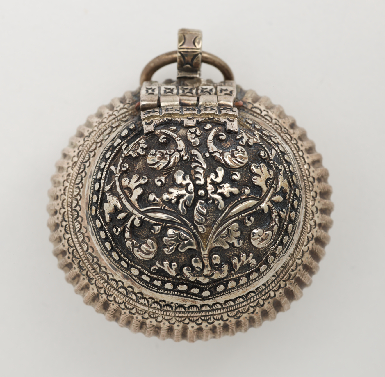 Rounded metal container with raised floral designs. A small circular metal ring attached to the top.
