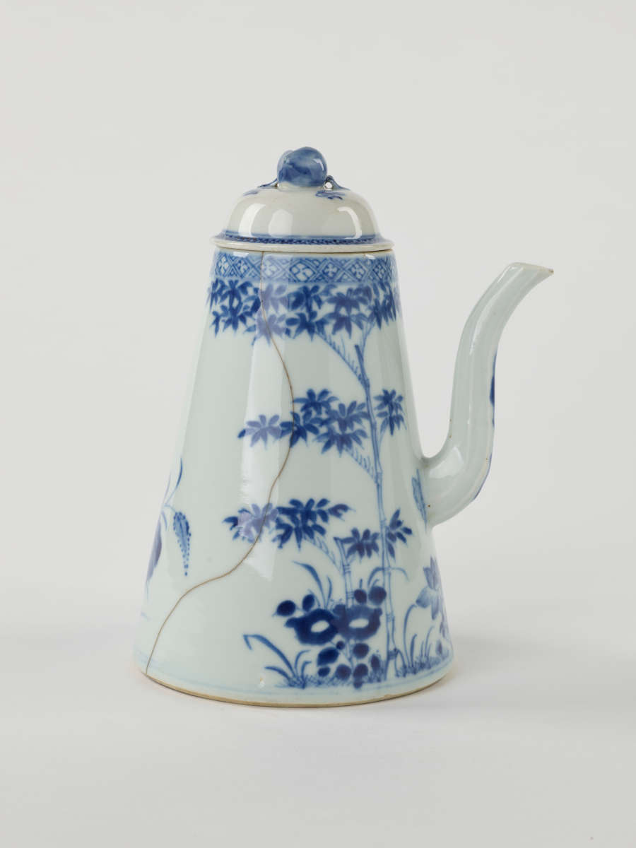 A white and blue teapot with floral decorations, a lid with a small semi spherical finial, spout, and a handle which is located approximately 90 degrees from the spout.