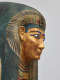 Side view of a coffin with a gilded face, beard, blue outlined eyes and a blue-black headdress with gold detailing. 