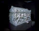 A marble coffin with deep-set carved figures engaged in battle, displayed on a pedestal in a dimly lit museum. 