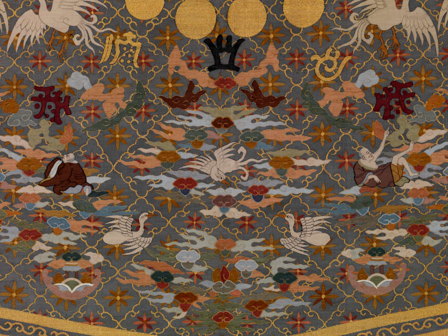 Detail of the robe’s back, featuring densely-packed  and symmetrically-arranged illustrations of birds, clouds, robed humans, golden and black symbols, golden circles and floral motifs against a background of layered patterns.