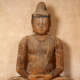 A close-up of a weathered wooden Buddha statue with a serene expression and closed eyes. 