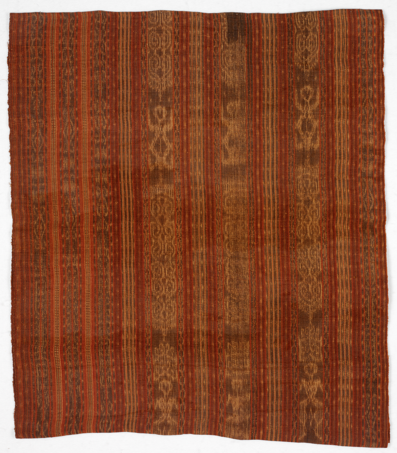 Rectangular woven textile on a white background with deep orange, red and gold tones. Features vertical stripes with intricate details bordering symmetrical abstract patterns on a soft, lustrous surface.