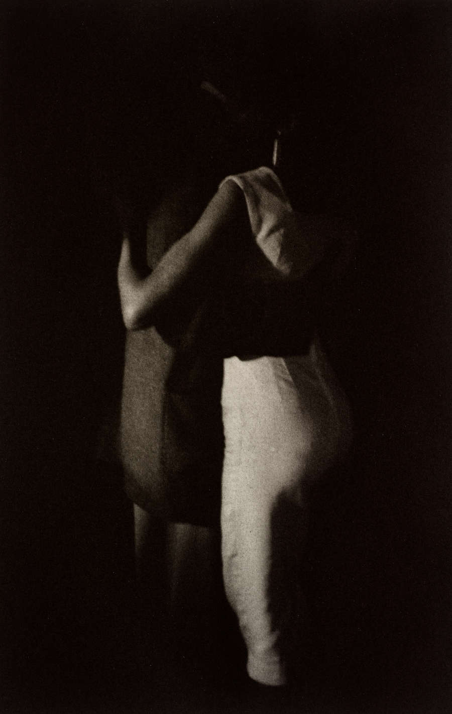 Black and white photo of two people dancing together, their arms around each other. Their faces and much of their bodies are completely obscured by shadows.