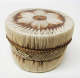 Cylindrical lidded leather box with cross-hatching and linear stripe patterns woven in white and brown straw. The brown rimmed lid has a central floral motif woven atop it.