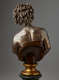 Back view of a bronze bust highlighting hair in twists and sculpted shoulder blades exposed above a dark strapless top cut off diagonally and mounted on a gold base.