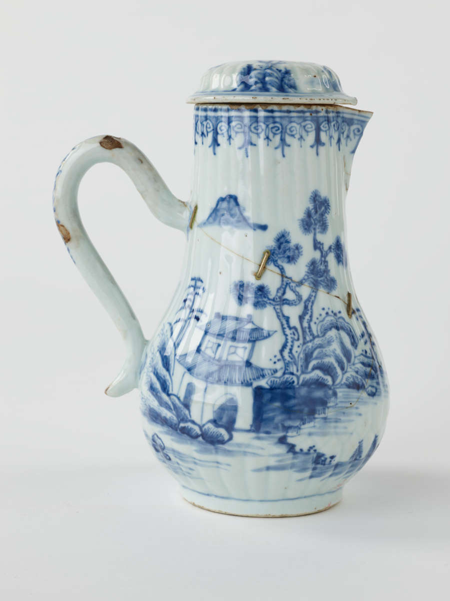 A white chocolate pot with blue decorations depicting floral and architectural elements.