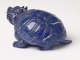 A back view of a blue sculpture of a horned tortoise, whose surface is covered with carved geometric patterns.