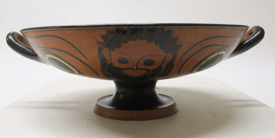 Terracotta and black cup with a wide mouth, short black neck, and orange base. One side features a bearded man flanked by two circular motifs rendered in black and white. 