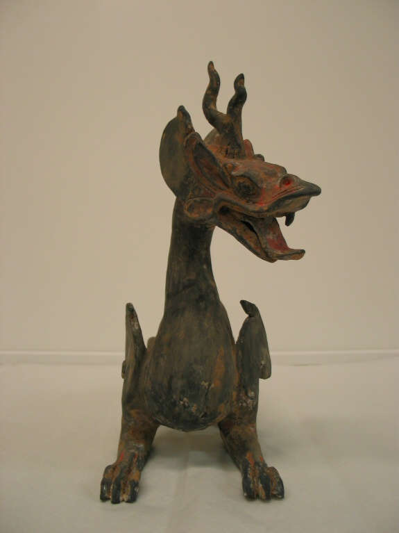 Front-view of an arched four-legged dragon with a lean body, open mouth, horned head, and sharp teeth, looking rightwards. The paint has worn into patches of browns and reds.