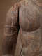 Close up of the torso of a weathered wooden Buddha statue, with a cracked chest and arm with faded carved details.
