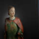 A weathered wooden statue of a figure with a solemn expression, with red and green drapery.