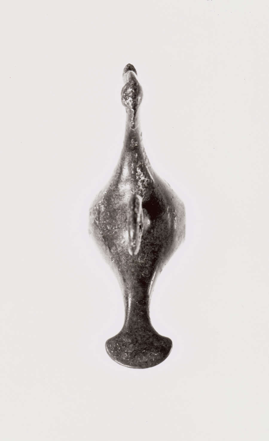 Top view of a silver figurine of a bird, with a large round bellow and thin slender neck, and tail that narrows and flares outwards. 