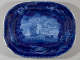 A deep blue ceramic platter with a central illustration of a large ship, framed by a border of seashells, coral, and marine motifs.