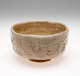 A bowl with undulating sides and rim. Cream and brown colored with a crackled surface and abstract designs scratched into the surface.