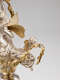 A cherub with small gold, feathered wings holds the end of a leafy garland, perched upon a larger silver-robed figure with butterfly-like gold wings. 
