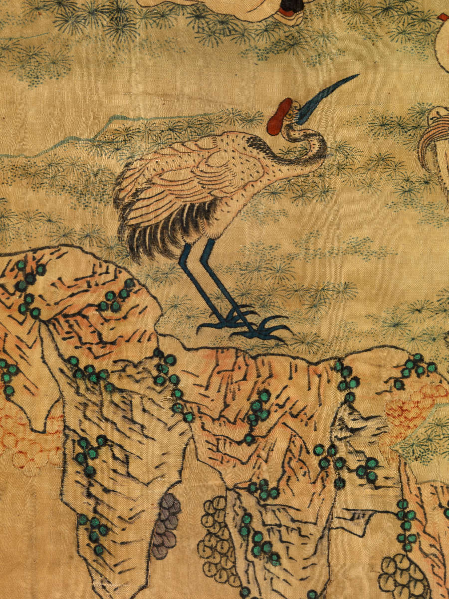 Detail showing a bird with a long slender neck, beak, and legs facing rightwards standing on the grassy edge of a cliff.