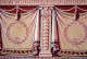 Flat wall detail featuring draped curtains that appear three-dimensional, laurel wreaths, decorative classical columns, and tassels, all in warm sepia tones.