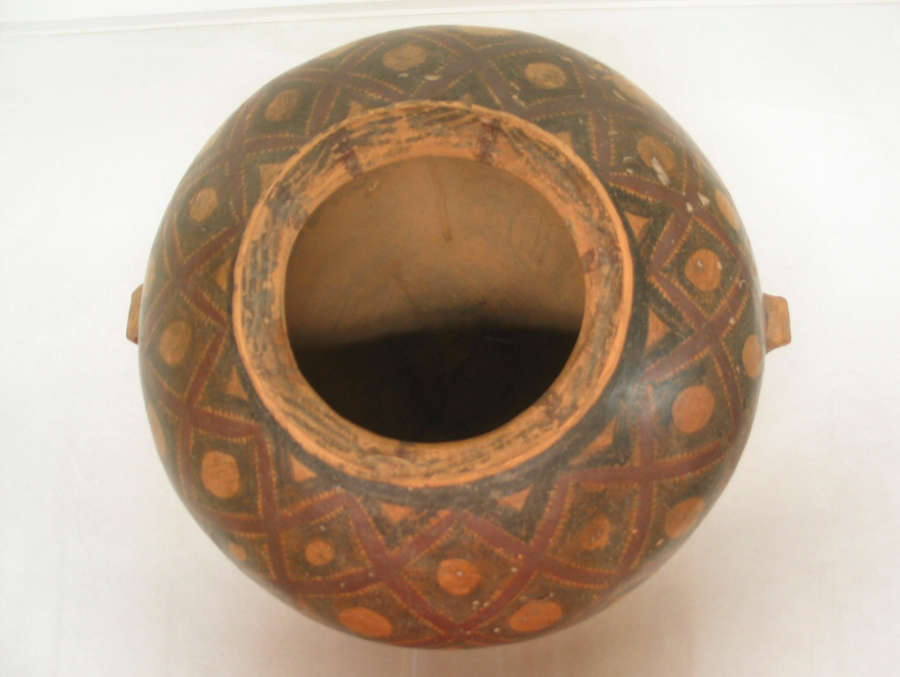 A top-down view of a large ceramic vessel with a wide, circular opening and hollow interior, decorated with red and black geometric patterns.