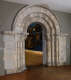Stone doorway with a rounded arch, framed by small columns topped with decorative carved designs.