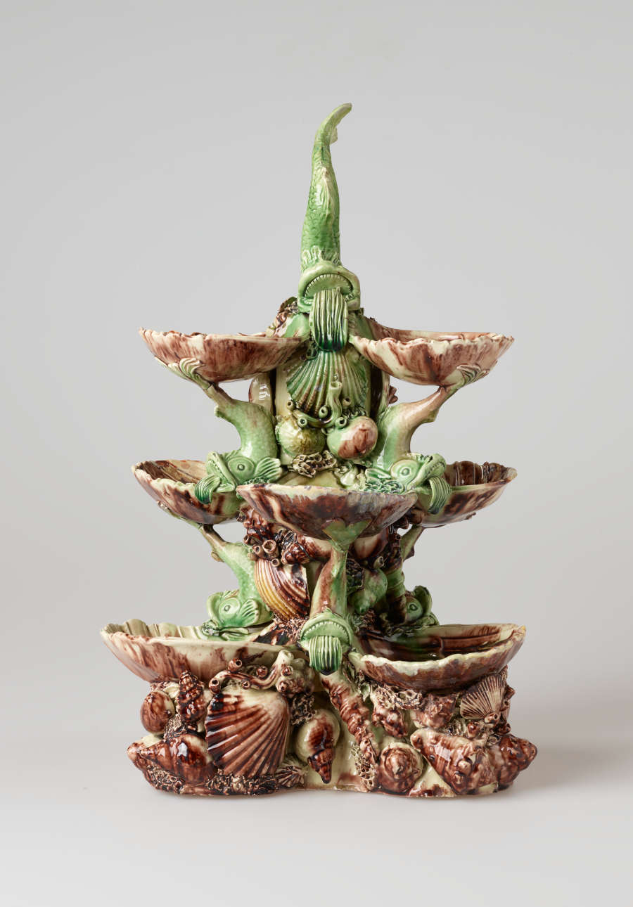 An elaborate, sculptural, three-tiered dish. Colored in brown, green, and cream with floral decorations as well as sculpted fish decorations.