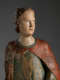A weathered wooden statue of a figure with a solemn expression, with red and green drapery.