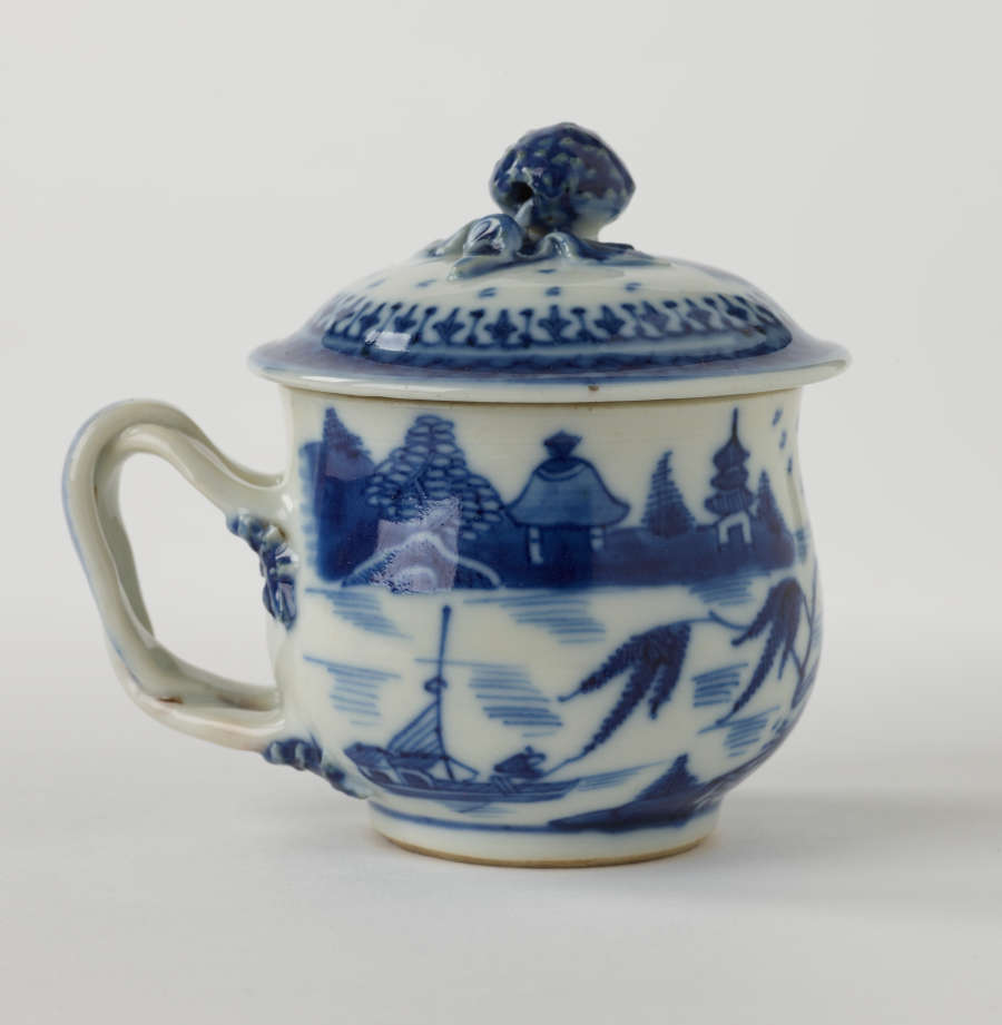 A covered cup with a sculptural swirled handle and blue architectural, floral, and scenic decorations.