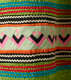 Another detail of the pattern. A thick strip of off-white with pink and black rectangles woven through it is surrounded by wavy horizontal red, blue, green, white, and purple stripes. 
