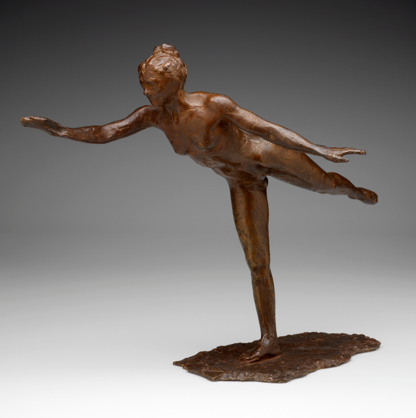 Detailed bronze sculpture of a female dancer balanced on her right foot. With her right arm outstretched and her left leg and arm raised behind, frozen in a pose.