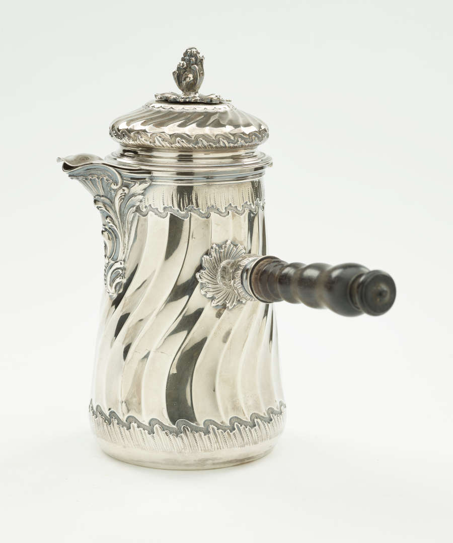 A silver chocolate pot with a decorative swirled body, lid, and fruit wood handle.