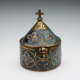 Copper box with cylindrical bottom and conical lid with gold and blue enameled geometric and floral patterns, topped with a carved cross.