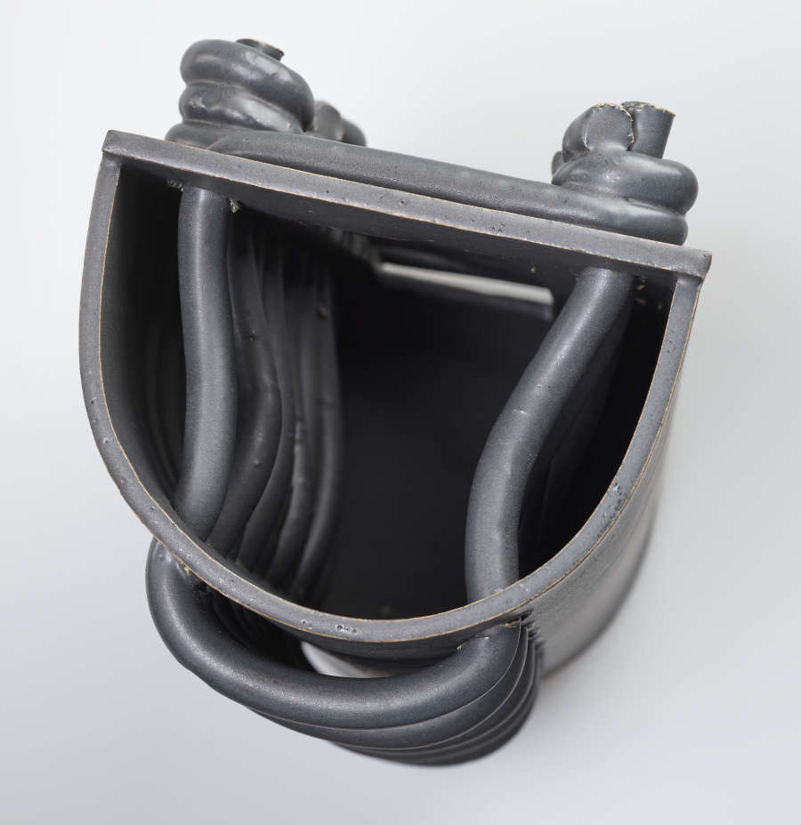 A top-down view of a circular, gray, open-top, ceramic sculpture. Interlaced coils are threaded through the center and protrude from facing sides. One side features knots while the other, loops.