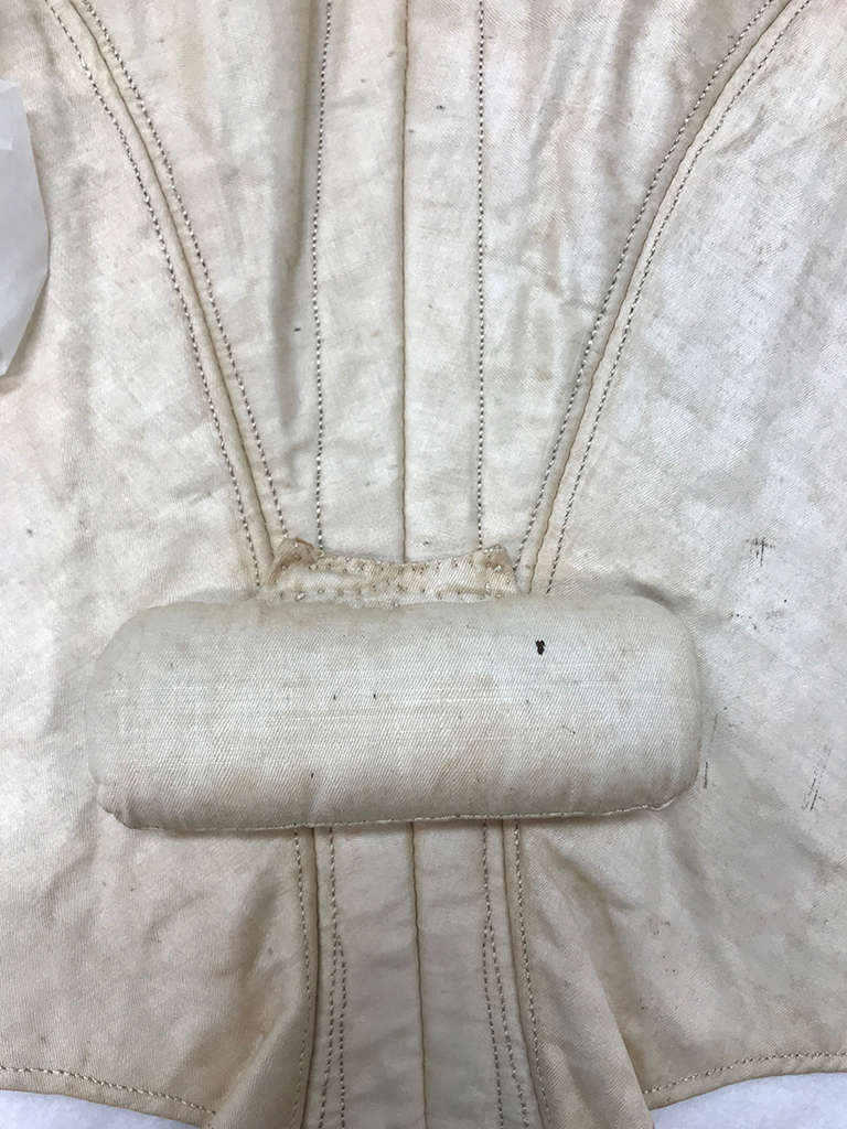 A padded fabric roll sewn onto an aged, cream-colored textile showing boning channels and visible stitching. 