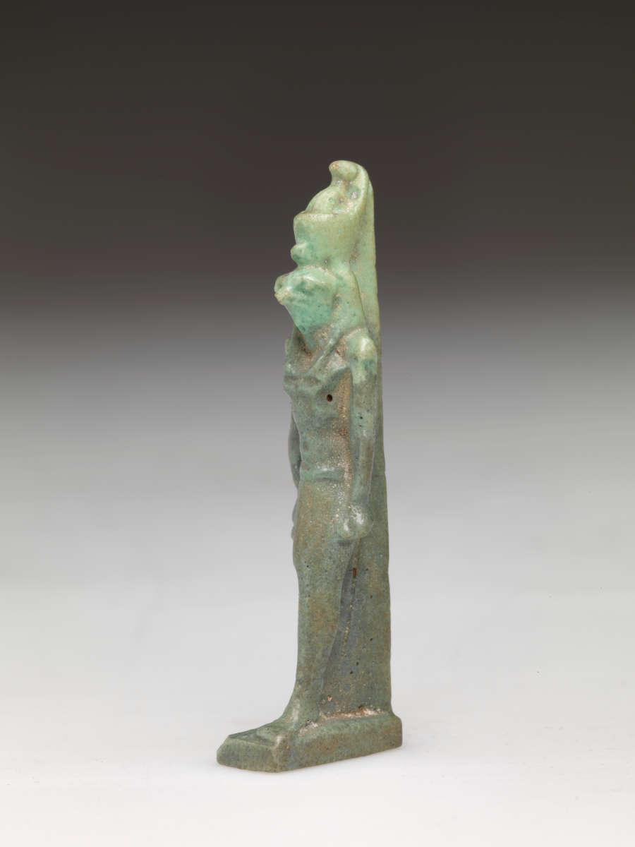 Partial side-view of light-jade sculpture of a standing person with a tall head, narrow torso, arms straight. The bottom half is a darker jade while the headdress is quite pale.