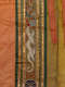 An embroidered white dragon-like creature puffs colorful flames above blue waves, framed vertically between gold and green bands on orange silk folded in front of yellow inside lining. 