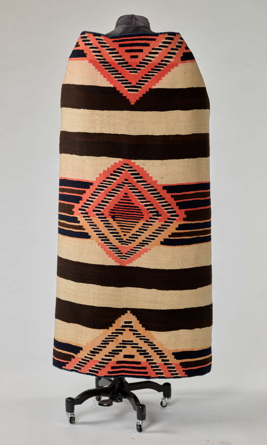 Back of a black and cream striped woven blanket with pink and yellow geometric patterns. The blanket has a stiff quality, creating an upright collar when draped around a mannequin.