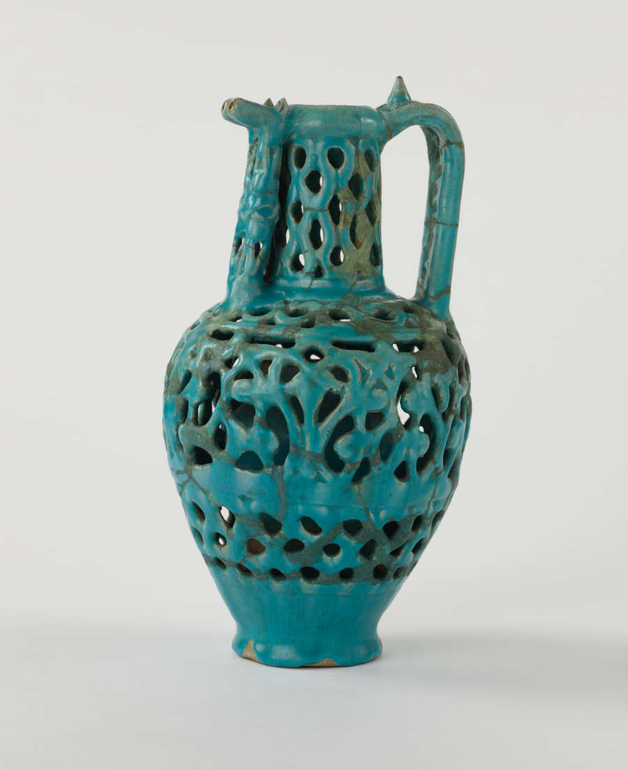 A turquoise ewer with cut out decorations and a sculptural spout and handle.