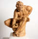 A realistic terracotta statue depicting a muscular, bearded man sitting in a dynamic pose and leaning over to hold a vessel with a creatures face situated between his legs. 