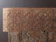 A close-up of an intricately carved wooden corner with repeating geometric patterns and swirling motifs, with part of an unfinished wooden edge visible. 