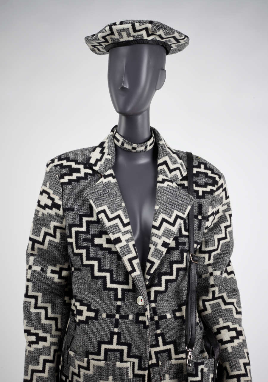 Close-up of a mannequin wearing a matching patterned, gray tweed jacket, hat, and choker. The blazer collar and choker touch, creating an illusion of seamless continuation between garments.