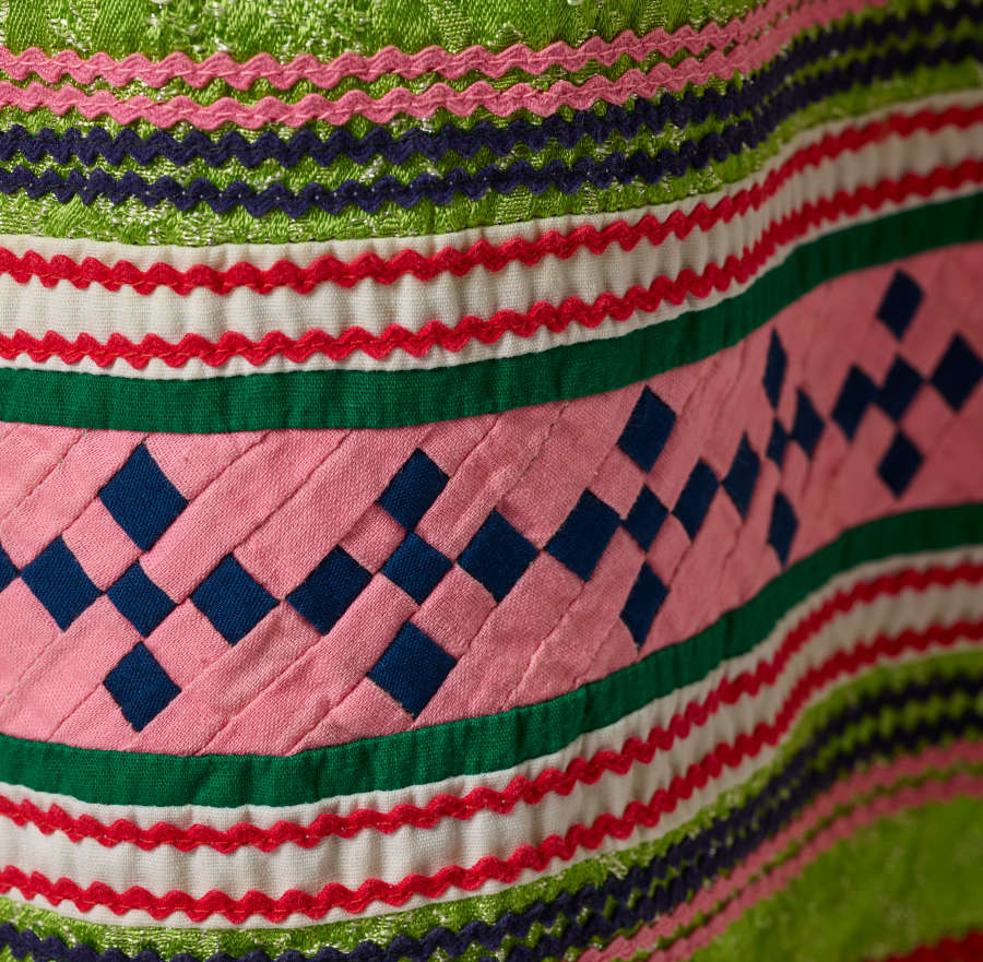 Detail of the pattern. A thick strip of pink with blue squares woven through it is surrounded by wavy horizontal green,white, and red stripes. 