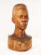 Slightly angled view of a glossy wooden bust depicting the head of a male figure with afrocentric facial features. He has a stern expression and an intense gaze.