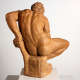 Realistically carved terracotta sculpture depicting the back of a muscular man leaning over while sitting, his bent arm supporting him against a rough pedestal he sits atop.