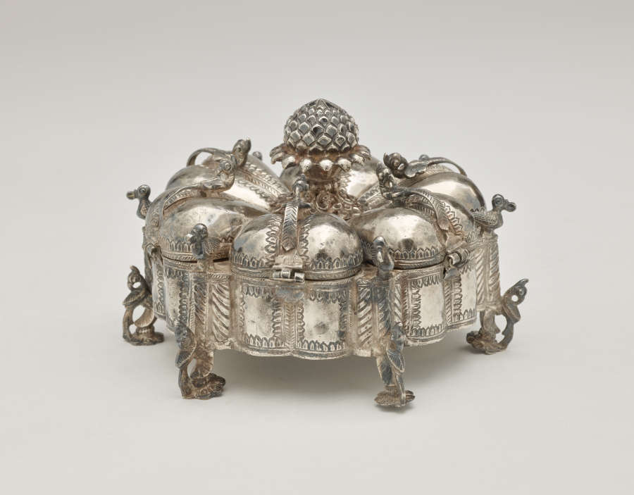 A dark silver spice box that is sculptural and has many different rounded compartments.
