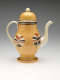 A yellow teapot with cream, orange, and brown circular designs dripping down at the bottom. Handle, spout, and final are cream colored.