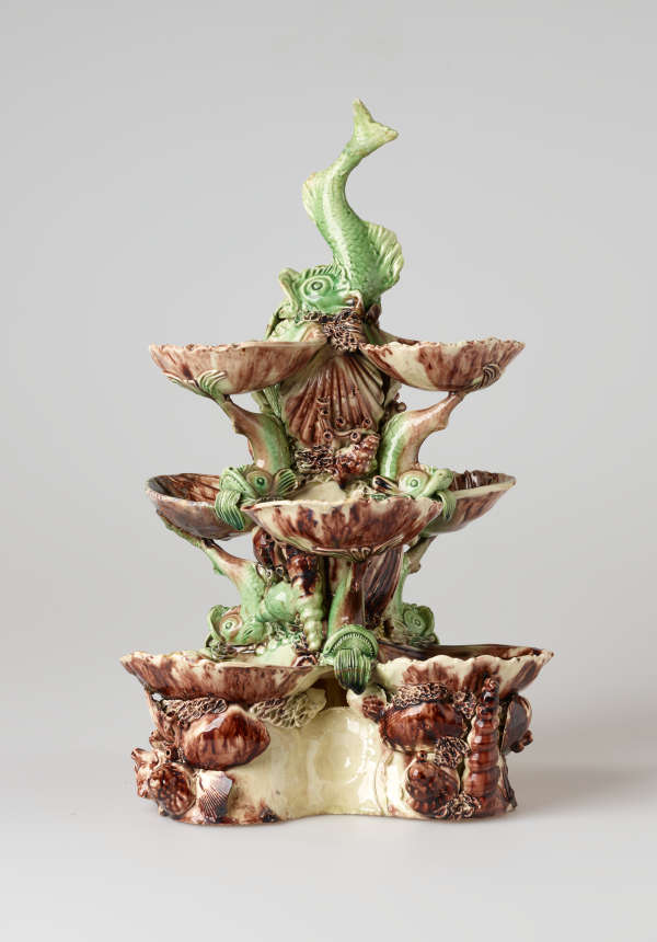 An elaborate, sculptural, three-tiered dish. Colored in brown, green, and cream with floral decorations as well as sculpted fish decorations.