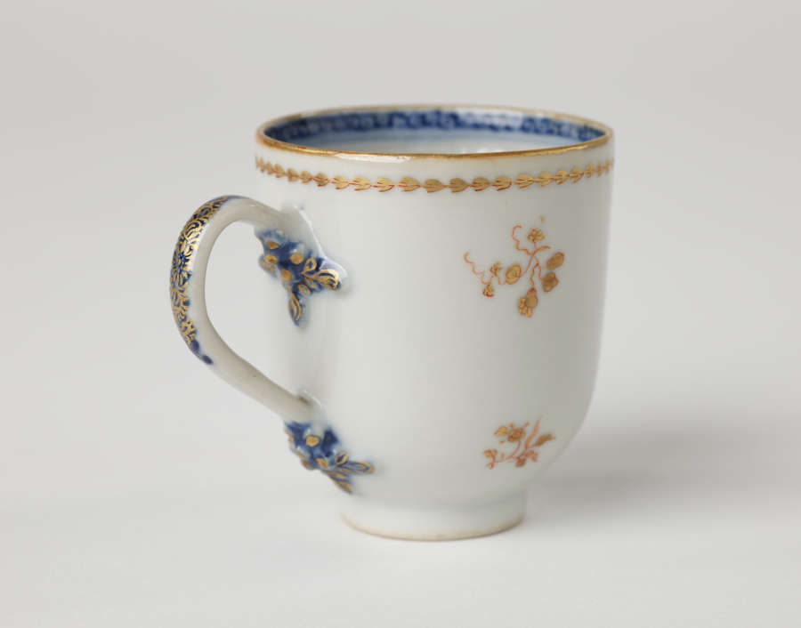 A cup with blue and gilded decorations along the outside and inside of the rim, body, and handle.