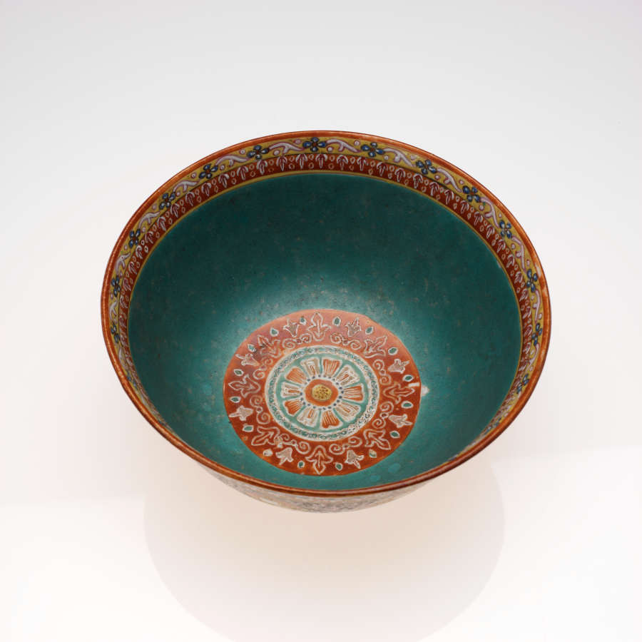 Top view of a circular bowl, showing its turquoise interior which features a red and golden patterned rim, and a concentrically patterned, red, orange, white, and turquoise base.