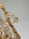 Close-up of a detailed silver figure in robes with flowing, wavy hair entangled in her fingers, holding up a gold, leafy garland with embedded roses across her face. 
