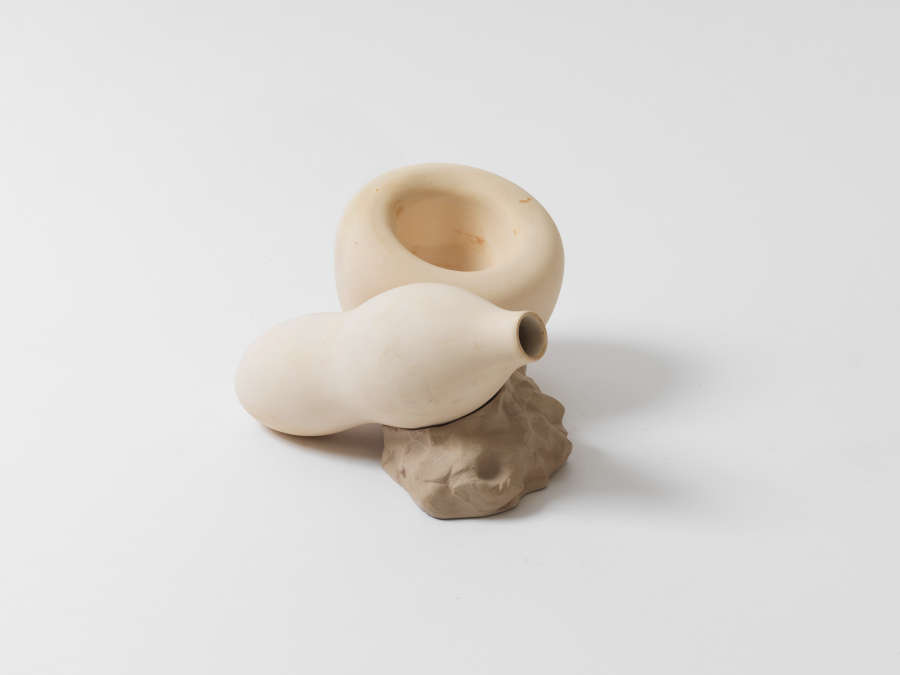 A sculptural piece with two cream-colored bulbous forms, one resembling a gourd and the other donut-like with a wide opening, resting together on an organic stone-like base.
